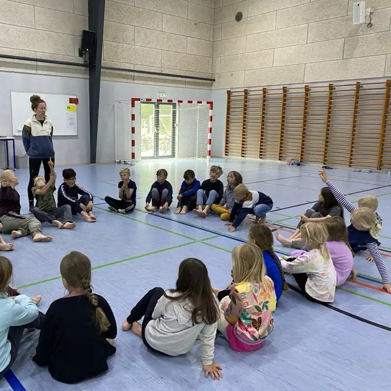 Elever sidder i en rundkreds i skolens sportshal på Grænseegnens Friskole